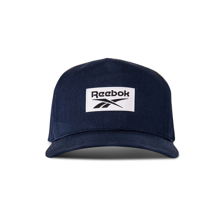 The Reebok Classic 5 Cap in navy blue features a white rectangular patch with the logo on the front panel, blending style and athletic comfort with moisture-wicking fabric.