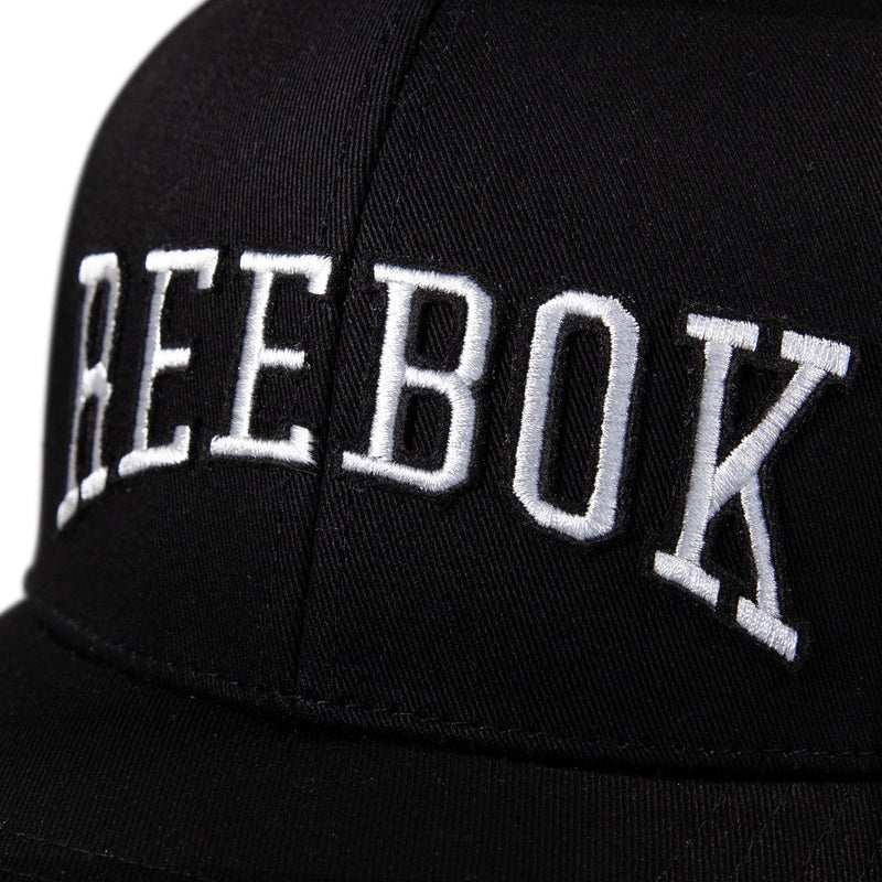 A close-up of the Reebok Gameday Cap, a black baseball cap featuring bold white "REEBOK" embroidery on the front.