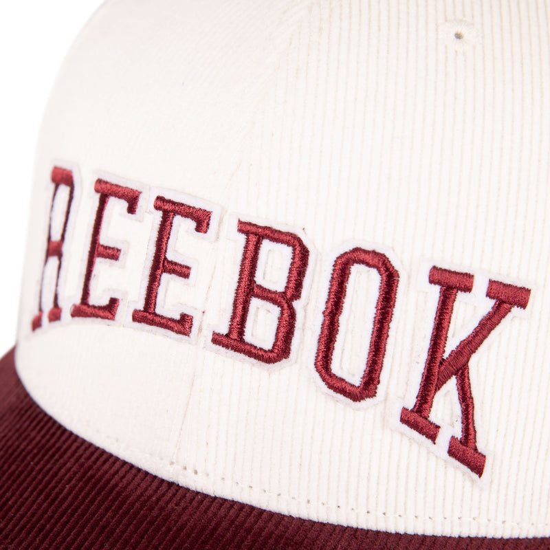 Close-up of the Reebok Corduroy Gameday Cap, a white corduroy baseball cap with a maroon brim and bold maroon REEBOK embroidery outlined in white on the front.