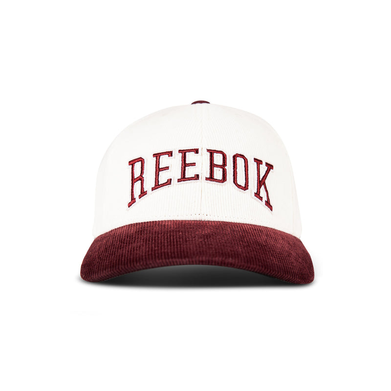 The Reebok Corduroy Gameday Cap is a white baseball cap featuring bold red REEBOK lettering on the front and a vibrant red corduroy brim, displayed from the front against a plain white background.