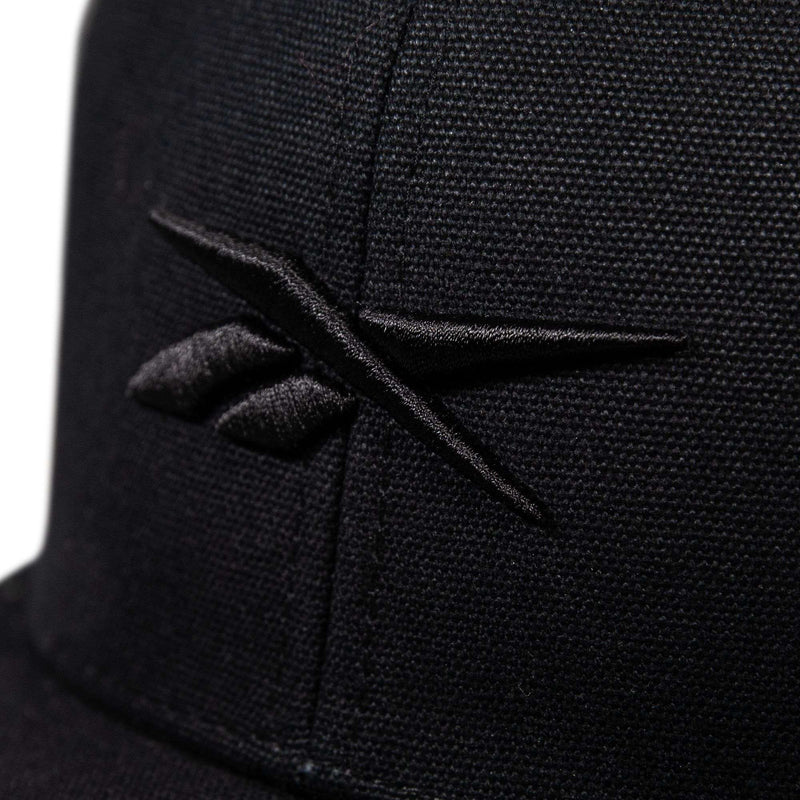 Close-up of the Reebok Embroidered Vector Trucker Cap in black, showcasing the embroidered black Reebok logo on the front with visible stitching and fabric texture.