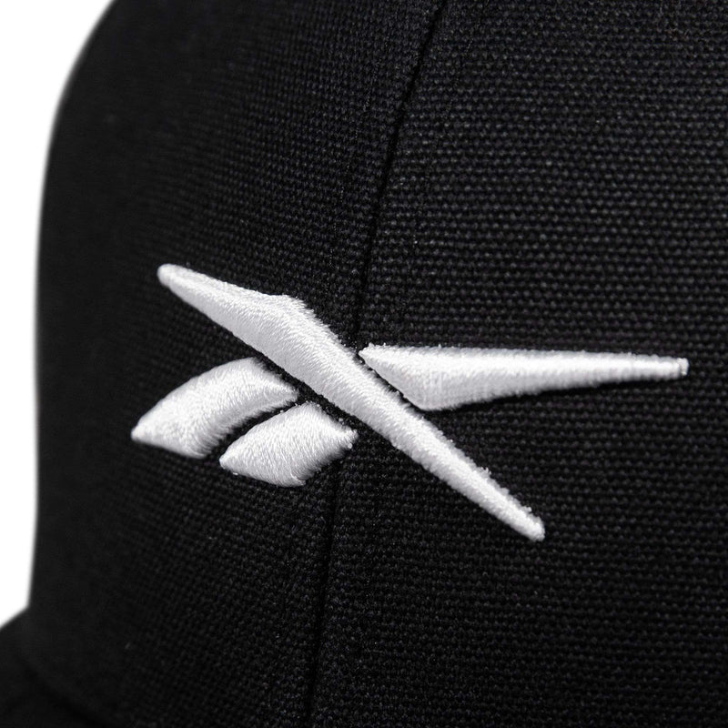 Close-up of the Reebok Embroidered Vector Trucker Cap, a black fabric hat with a white embroidered Reebok logo on the front.