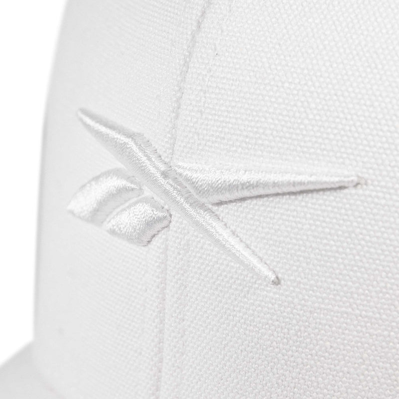 Close-up of the Embroidered Vector Trucker Cap by Reebok, showing a white fabric surface with the Reebok logo stitched in white thread.
