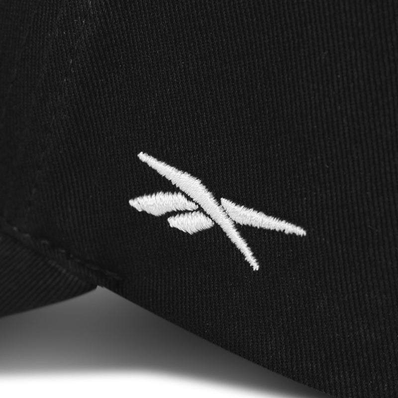 Close-up of the Reebok Chroma Cap, a black cotton twill hat with a white embroidered logo of two intersecting angled lines and an adjustable snapback for a custom fit.