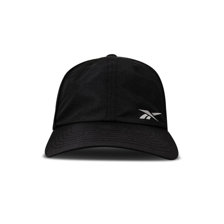 The Reebok Flow Piped Cap in black features a curved brim, a small white logo on the front left, and is made from recycled polyester with a moisture-wicking sweatband. Shown against a plain white background.