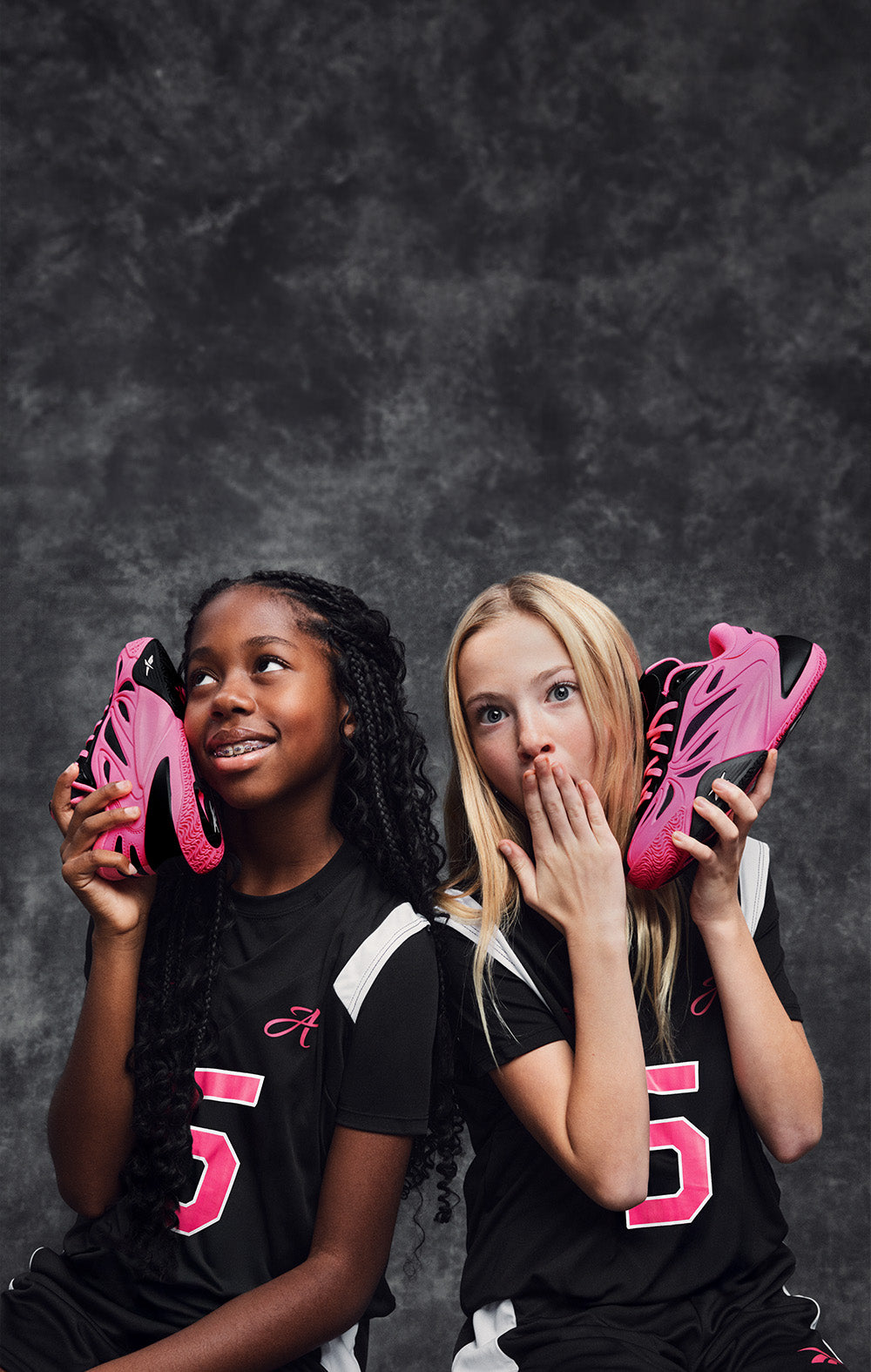 Two children holding pink sports shoes against a dark background