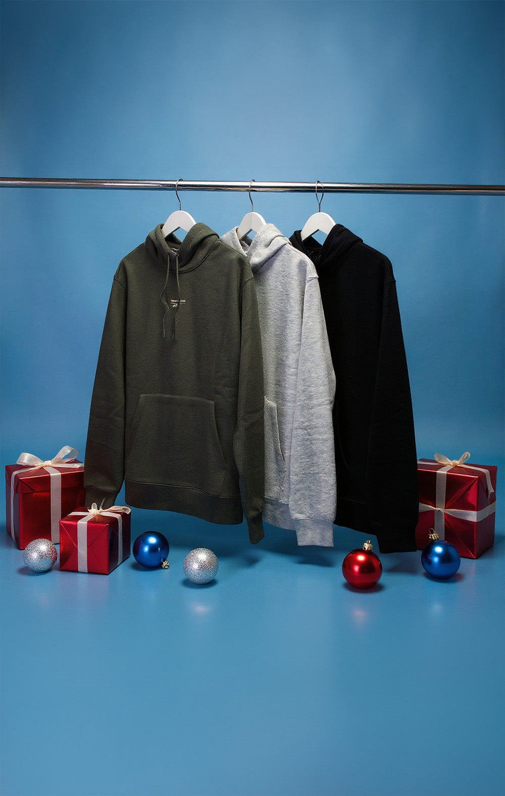 Three hoodies on hangers with Christmas presents and ornaments on a blue background