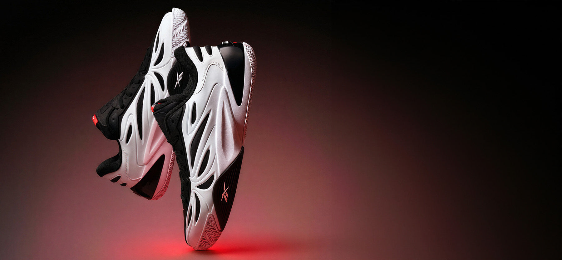 White and black sneakers with a glowing red sole on a dark background