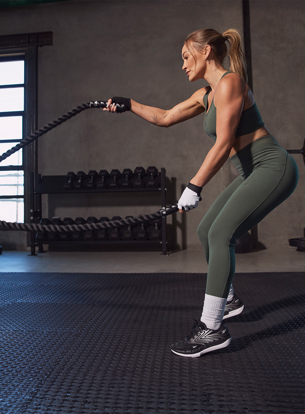Woman in green in a gym, wearing black reebok shoes, using ropes for exercise