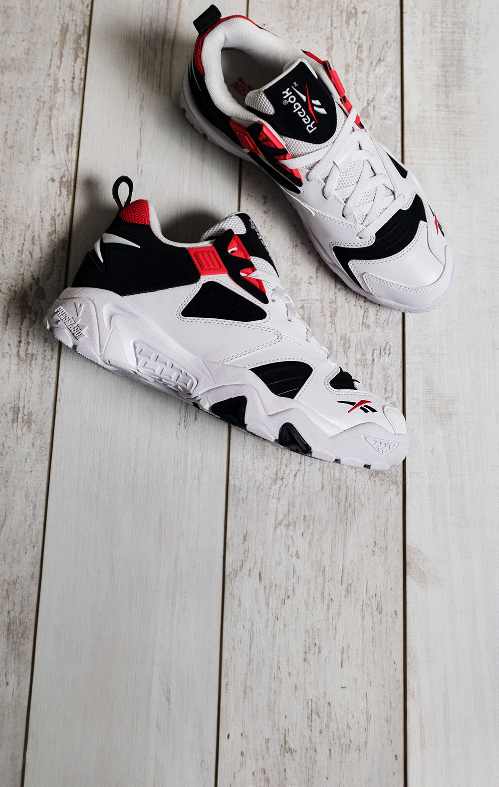 White sneakers with black and red accents on a wooden floor