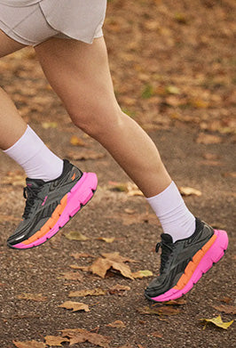 Person wearing black and pink running shoes on a leafy path