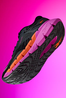 Black running shoe with pink and orange sole on a pink background