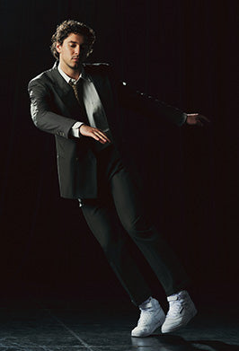 man in suit against a black background jumping in white reebok sneakers 