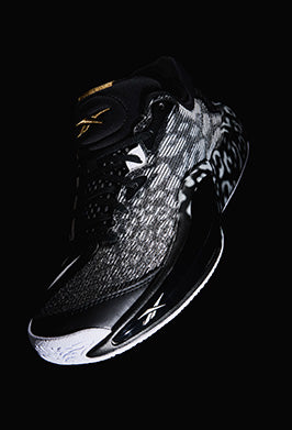 Black athletic shoe with white sole on a black background