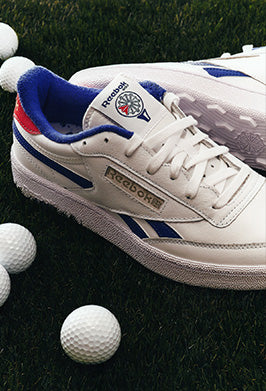 White Reebok sneakers with blue and red accents on a grassy background