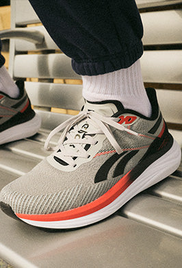 Gray running shoe with black and red accents on a metal bench