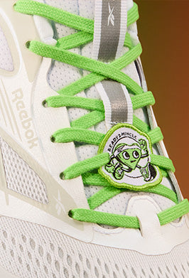White Reebok sneaker with green laces and a character charm on a blurred background
