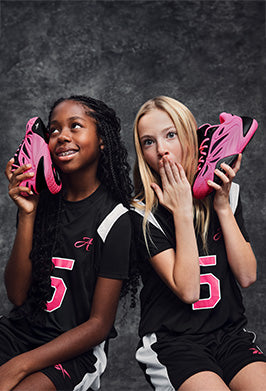 Two girls holding pink shoes against a dark background