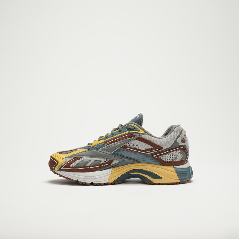 The Reebok Premier Road Ultra LTD Shoes are shown from the side, featuring yellow, blue, gray, and brown accents on a white background. This archival running sneaker includes a dual-density midsole for enhanced comfort.