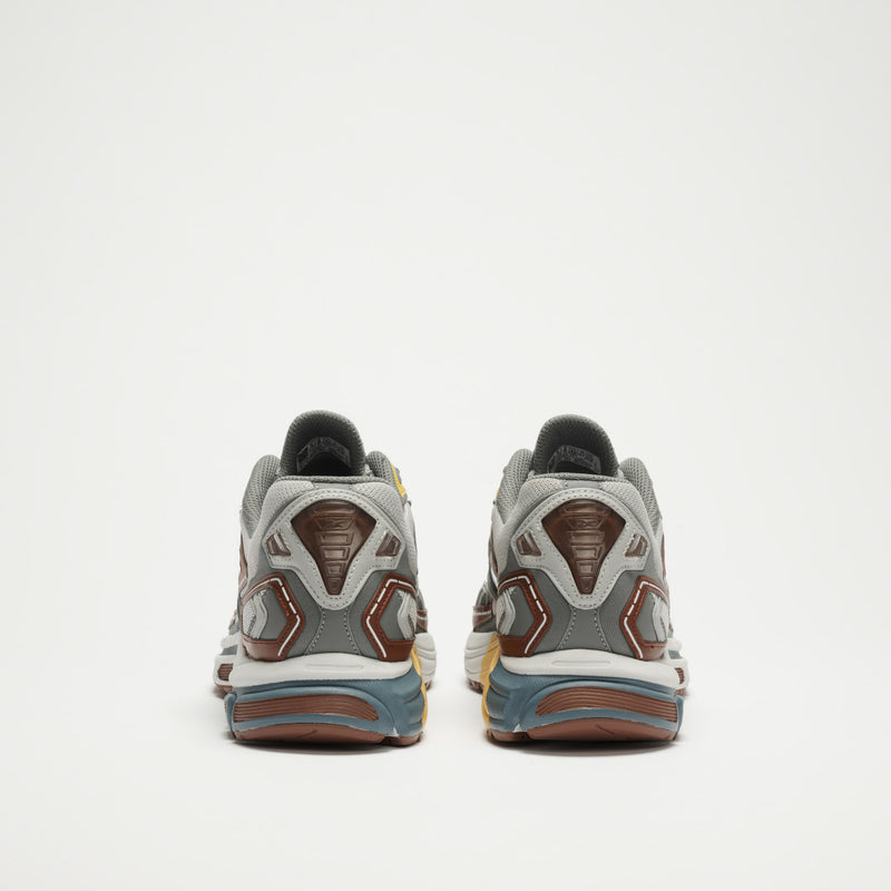 A pair of gray, brown, and blue Reebok Premier Road Ultra LTD Shoes is displayed from the back on a white background. The shoes have black and yellow accents, chunky soles, and a dual-density midsole for comfort.