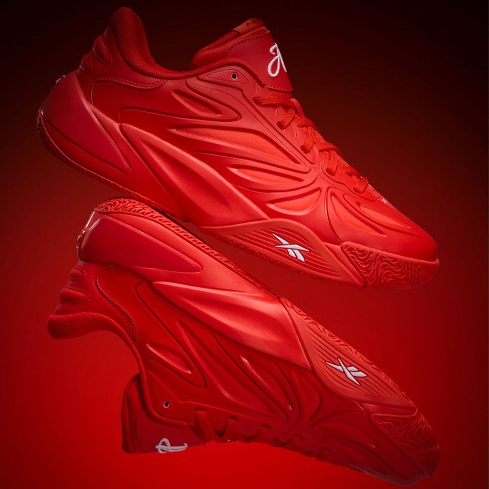Two vibrant red Angel Reese 1 Basketball Shoes by Reebok, featuring dynamic sculpted designs, white Reebok logos, and the Energy Return System, are showcased against a red gradient background, highlighting their superior texture and athletic details.