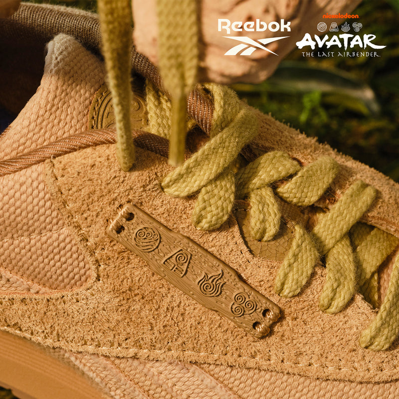 Tan Reebok x Avatar Classic Nylon shoes with sage green laces and a decorative lace charm featuring elemental symbols from Avatar: The Last Airbender.