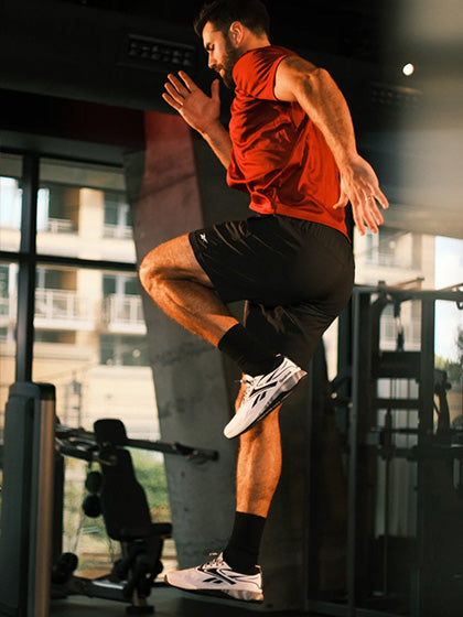 Man in red tank top and black shorts jumping in a gym.