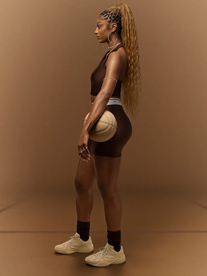 Person wearing a brown sports bra and black shorts on a brown background