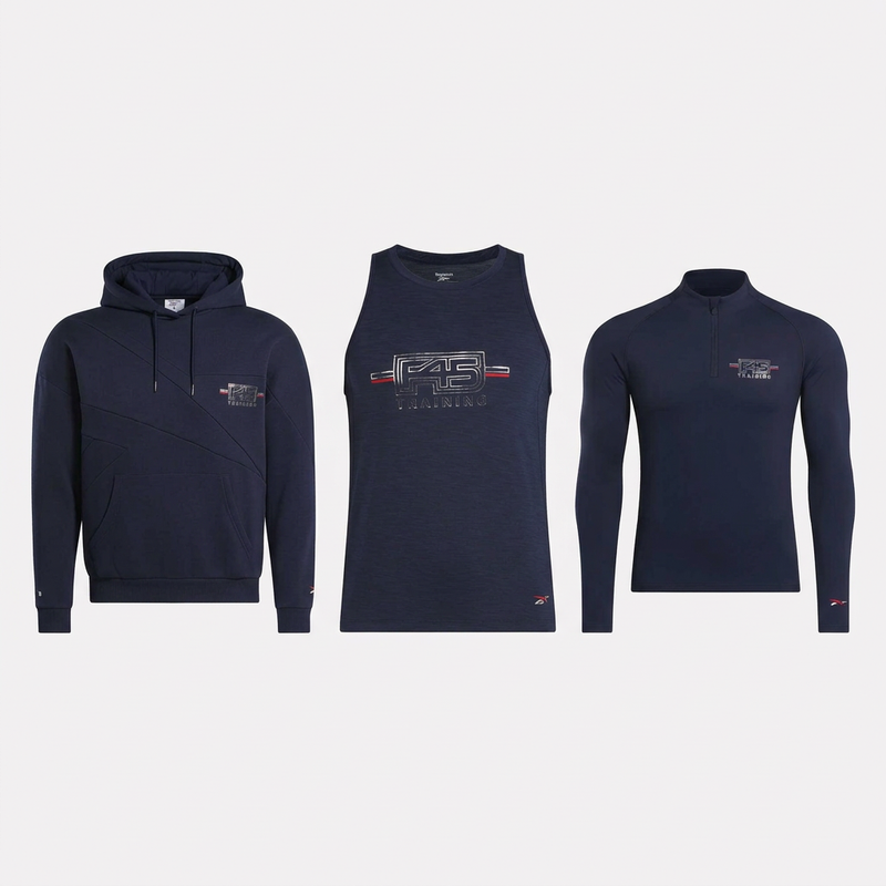 Three navy blue athletic tops from the Reebok Men's Layer Kit—a hooded sweatshirt, sleeveless tank, and long-sleeve quarter-zip—are lined up side by side, each featuring a small logo and “45” graphic for comfort during training.