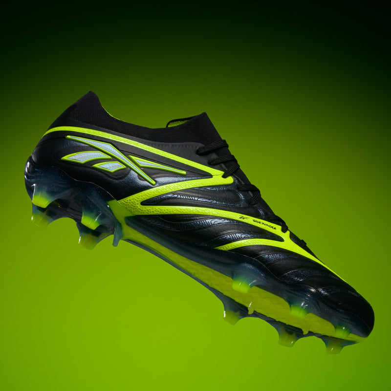 The Reebok Sidewinder 26 Elite FG Cleats, featuring a black design with bright yellow accents and neon yellow studs for firm grass, are presented on a gradient green background to showcase their sleek, modern look.