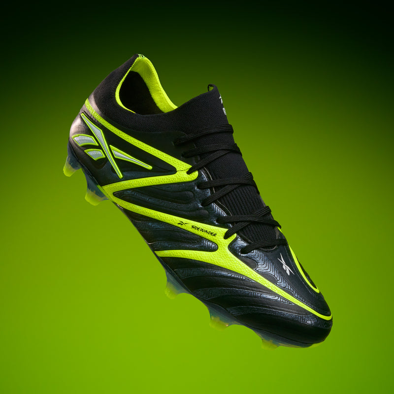 The Reebok Sidewinder 26 Elite FG Cleats are black soccer cleats with neon yellow accents, shown on a green gradient background. Designed for firm ground, they feature laces, textured details, and improved ball control.