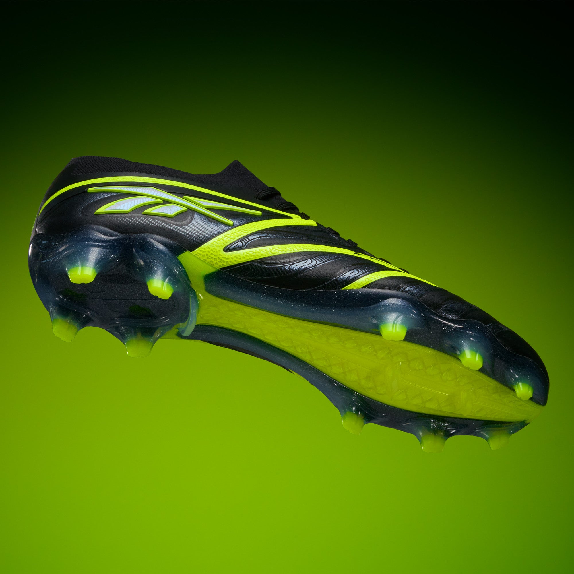 The Reebok Sidewinder 26 Elite FG Cleats in black and neon yellow are displayed from below on a vibrant green gradient, showcasing the firm ground sole and studs.