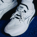 White athletic sneakers with white socks, shown in a close-up shot on a textured blue surface.