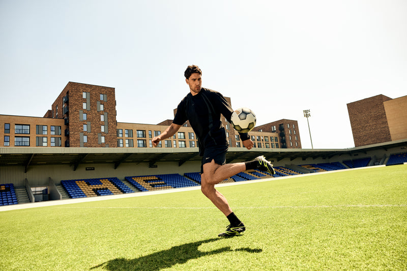 Dusan Vlahovic kicking a soccer ball in the Sidewinder Cleat, standing on a turf field on a sunny day