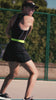 a woman wearing black tennis dress playing tennis on a court surrounded by trees