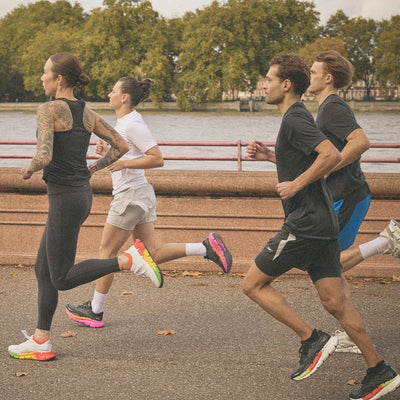 Four people running along a path by a river with trees in the background