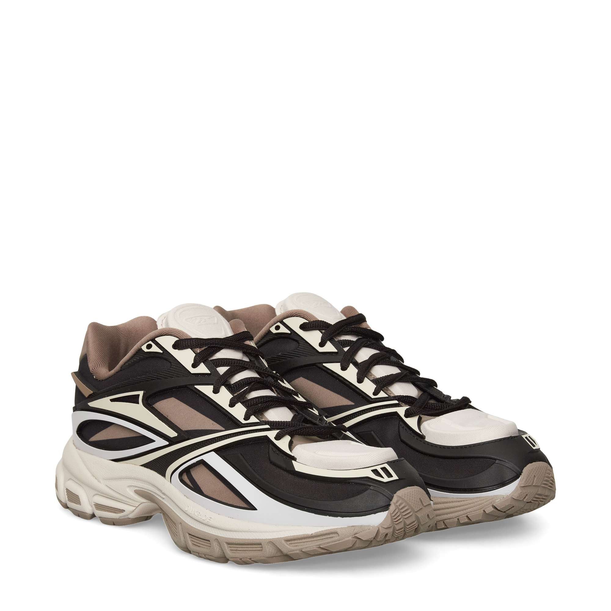 A pair of chunky, modern sneakers with a mix of black, white, brown, and beige panels, featuring thick soles and black laces, displayed against a plain white background.