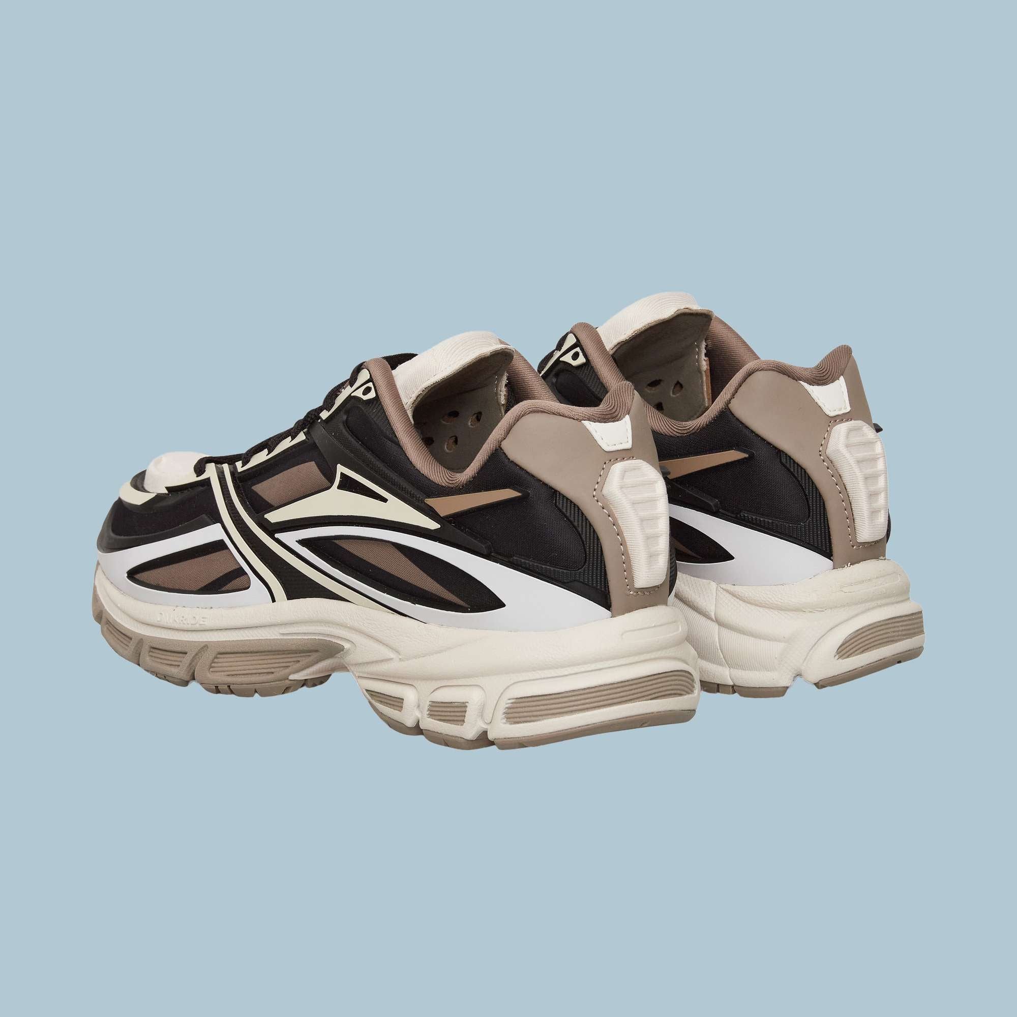 The Reebok Premier Road Modern Shoes are stylish black, white, and beige sneakers with thick soles and dynamic stripe designs, inspired by a futuristic look and shown against a light blue background.