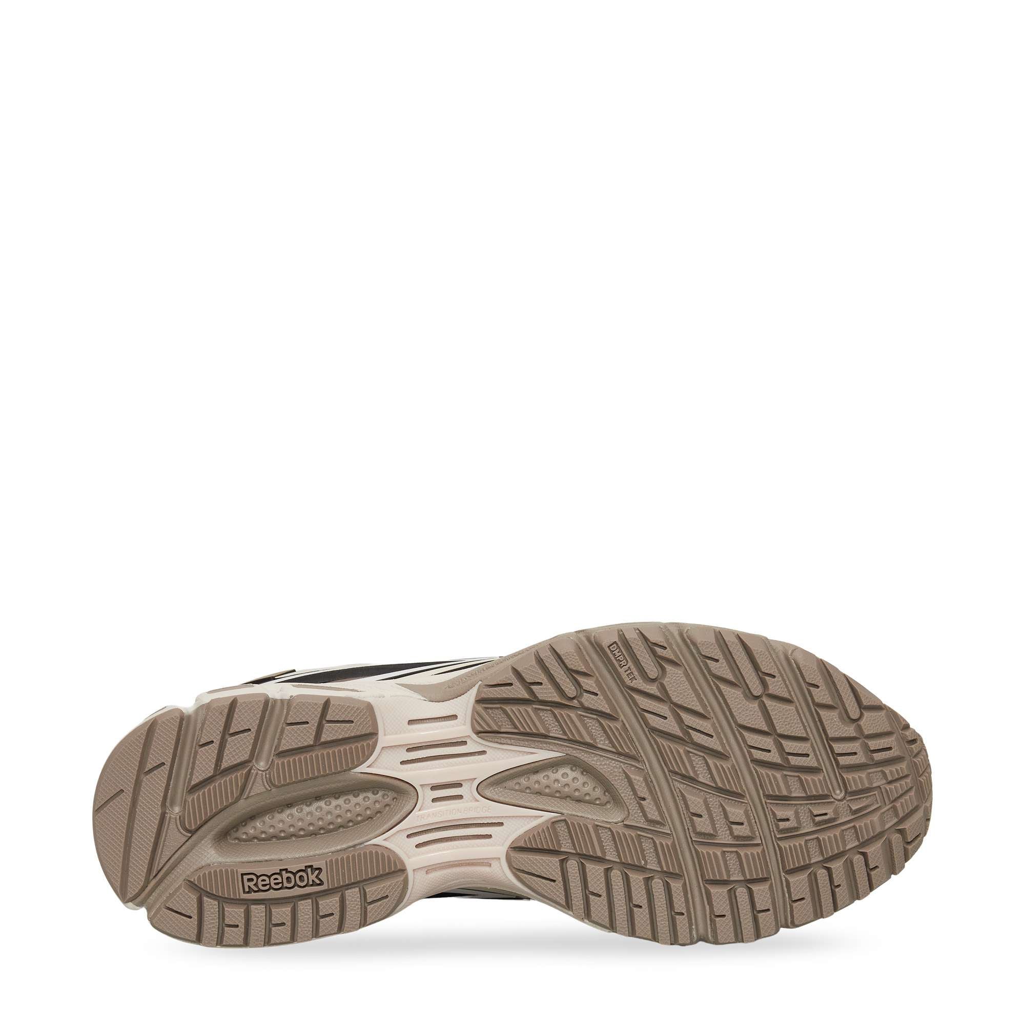 Bottom view of a Reebok sneaker showing a textured rubber outsole in light brown with various grooves and patterns for traction. The Reebok logo is embossed near the heel area of the sole.
