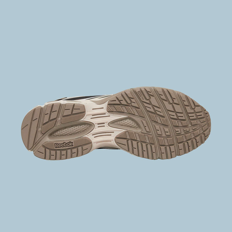 The image shows the beige, textured non-slip rubber sole of the Reebok Premier Road Modern Shoes, designed for traction and durability, set against a light blue background. These sneakers blend futuristic style with peak performance.