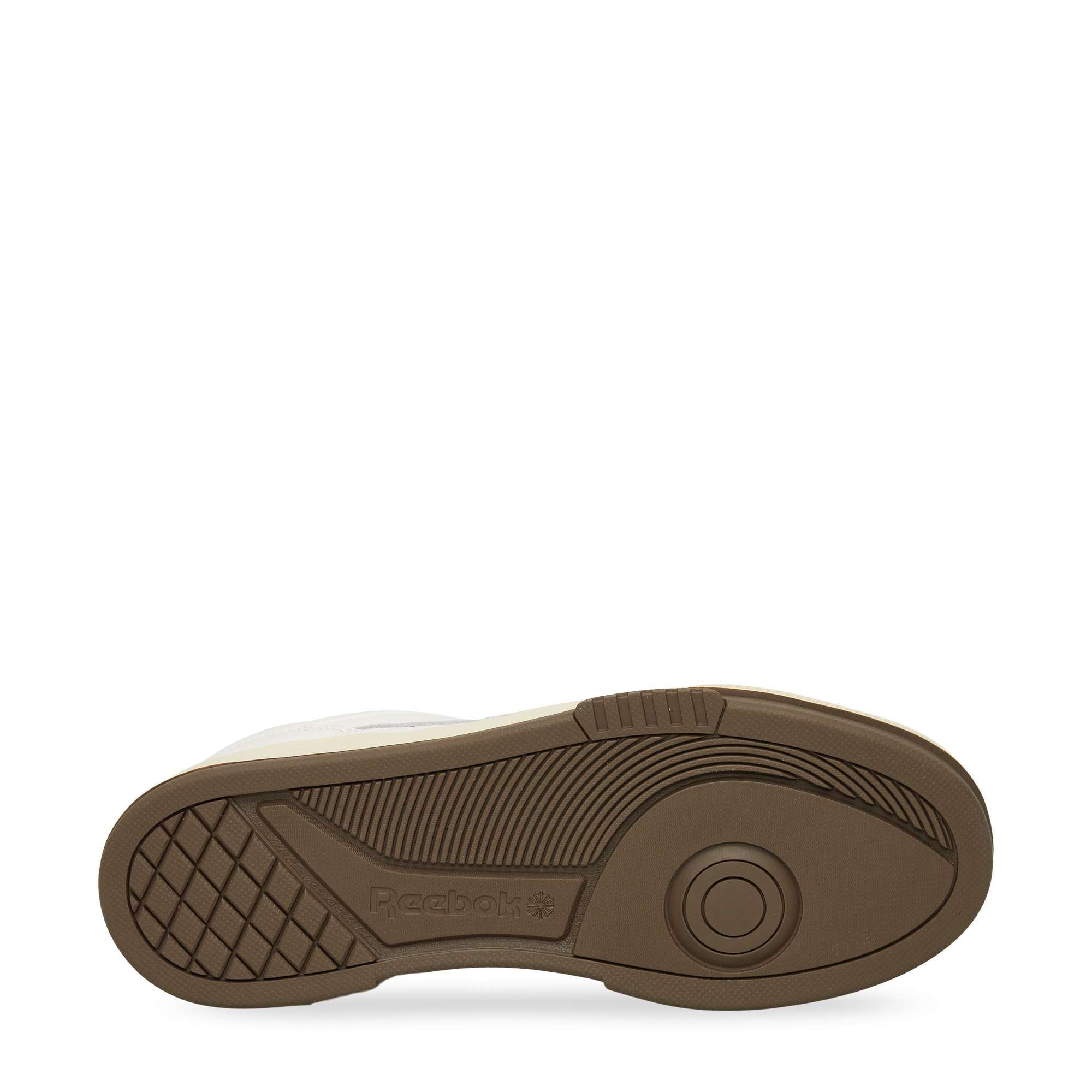 The image shows the brown rubber sole of a Reebok sneaker, viewed from the bottom, featuring textured grip patterns and the Reebok logo embossed near the heel. The sole is set against a plain white background.
