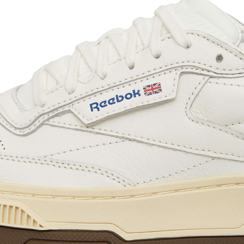 Close-up of a white Reebok Club C LTD shoe with textured leather, white laces, beige midsole, brown outsole, and the iconic Reebok logo—an updated take on this classic lifestyle sneaker.