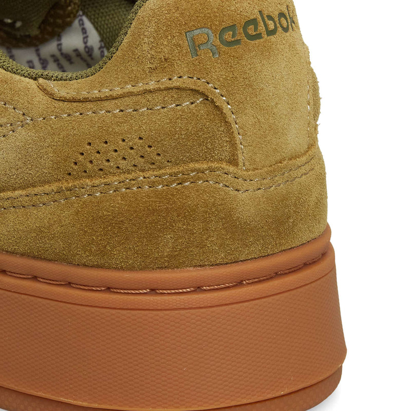 Close-up of the heel of a tan suede Reebok Club C LTD shoe, featuring gold branding, perforated accents, and a textured light brown rubber sole—a classic lifestyle style.