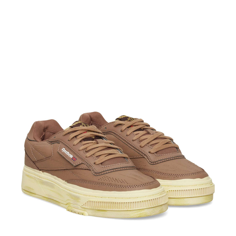 The Reebok Club C LTD Shoes, in brown with beige, vintage-look soles, feature laces and the signature logo on the side. Displayed against a white background, these sneakers offer a classic blend of comfort and timeless style.