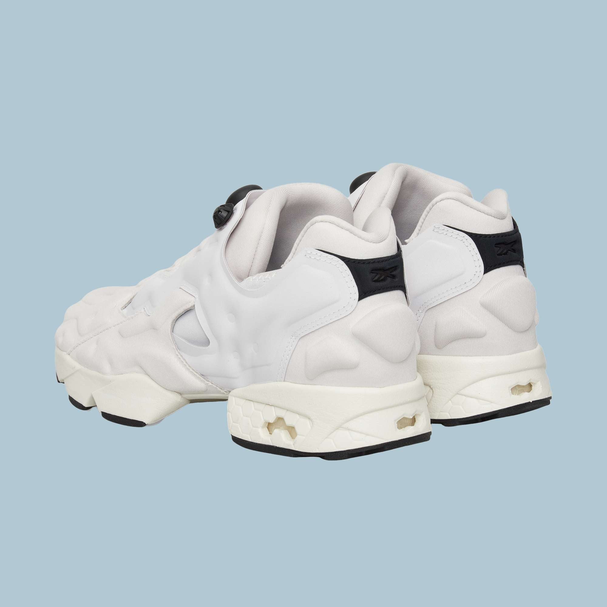 The Reebok Instapump Sliver Shoes, white with chunky soles, black heel accents, and cutout details featuring Hexalite cushioning, are shown from the back on a light blue background.