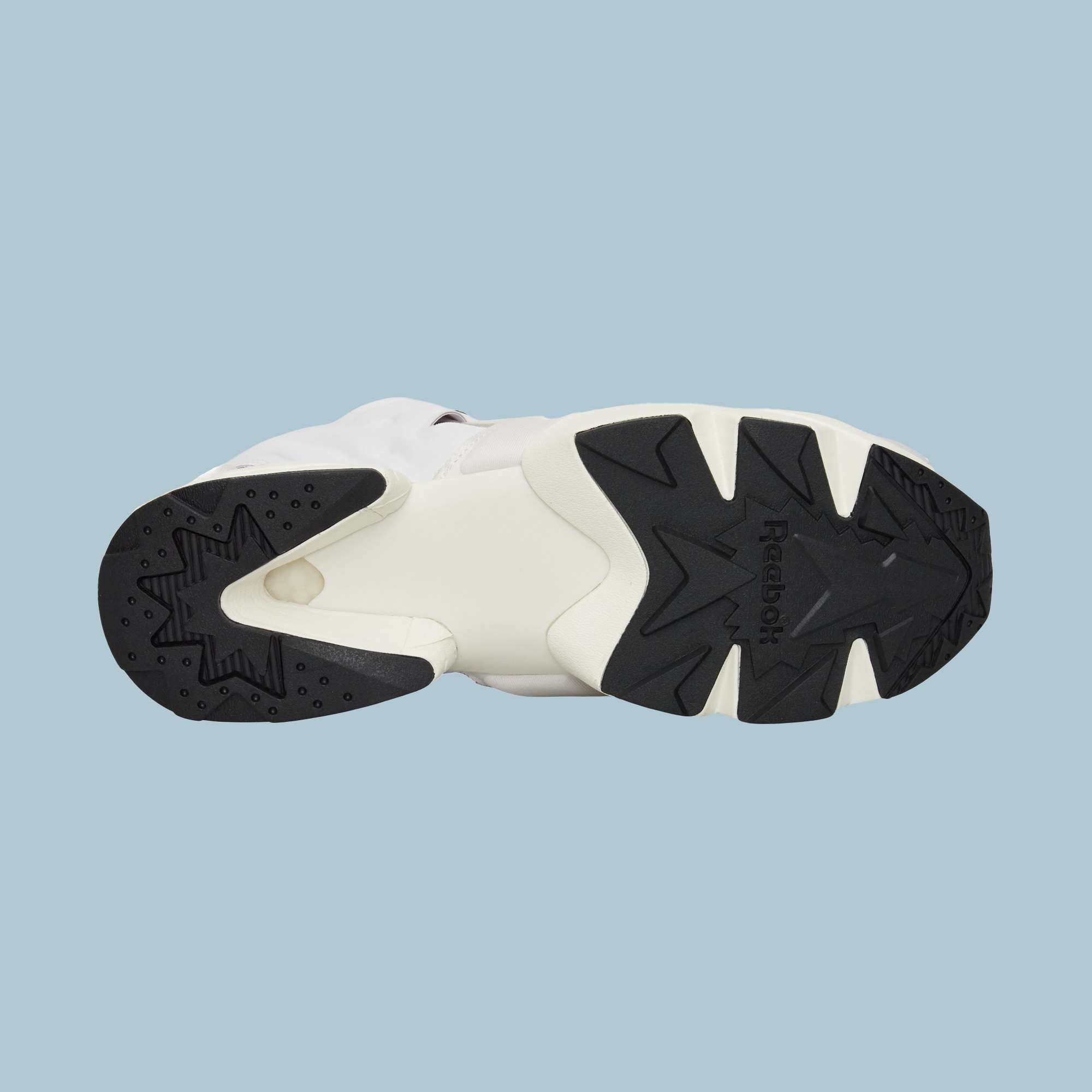 The image displays the sole of Reebok Instapump Sliver Shoes, with a mainly black and white geometric tread pattern for grip and Hexalite cushioning, set against a light blue background.