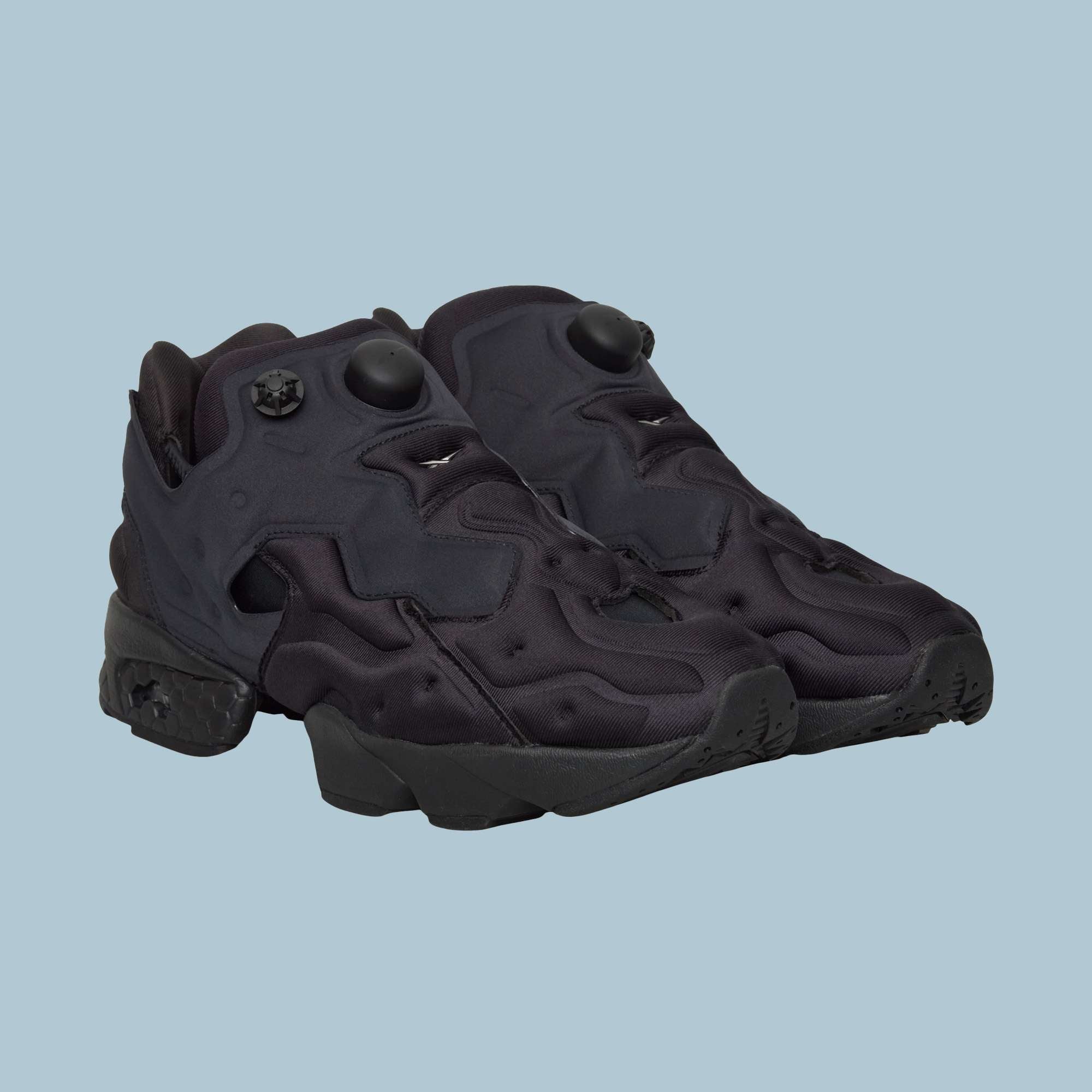 A pair of Reebok Instapump Sliver Shoes in black, showcasing a chunky design with textured soles and Hexalite cushioning, displayed on a plain light blue background.