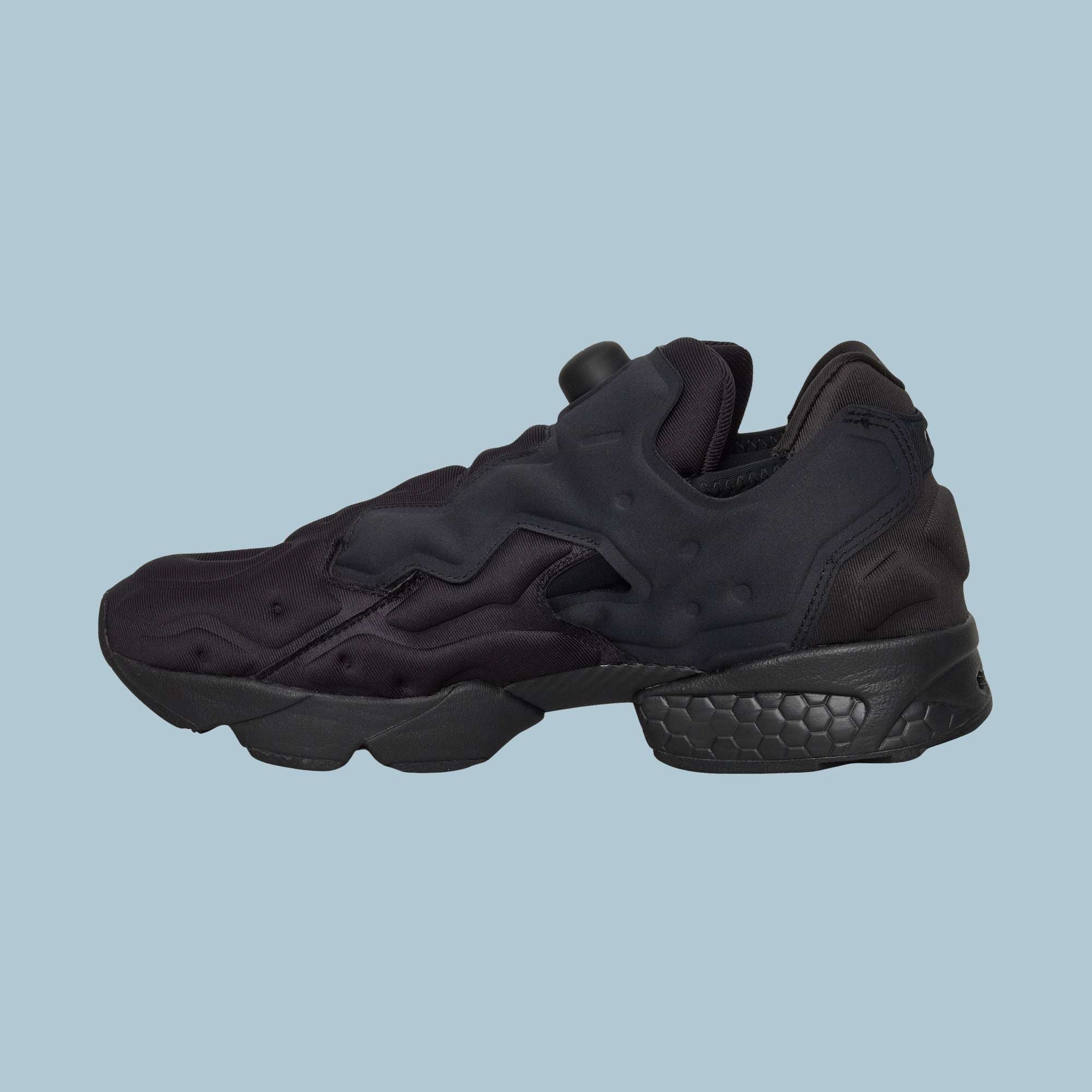 The Reebok Instapump Sliver Shoes are black sneakers with a chunky Hexalite-cushioned sole and wavy futuristic design, displayed on a solid light blue background.