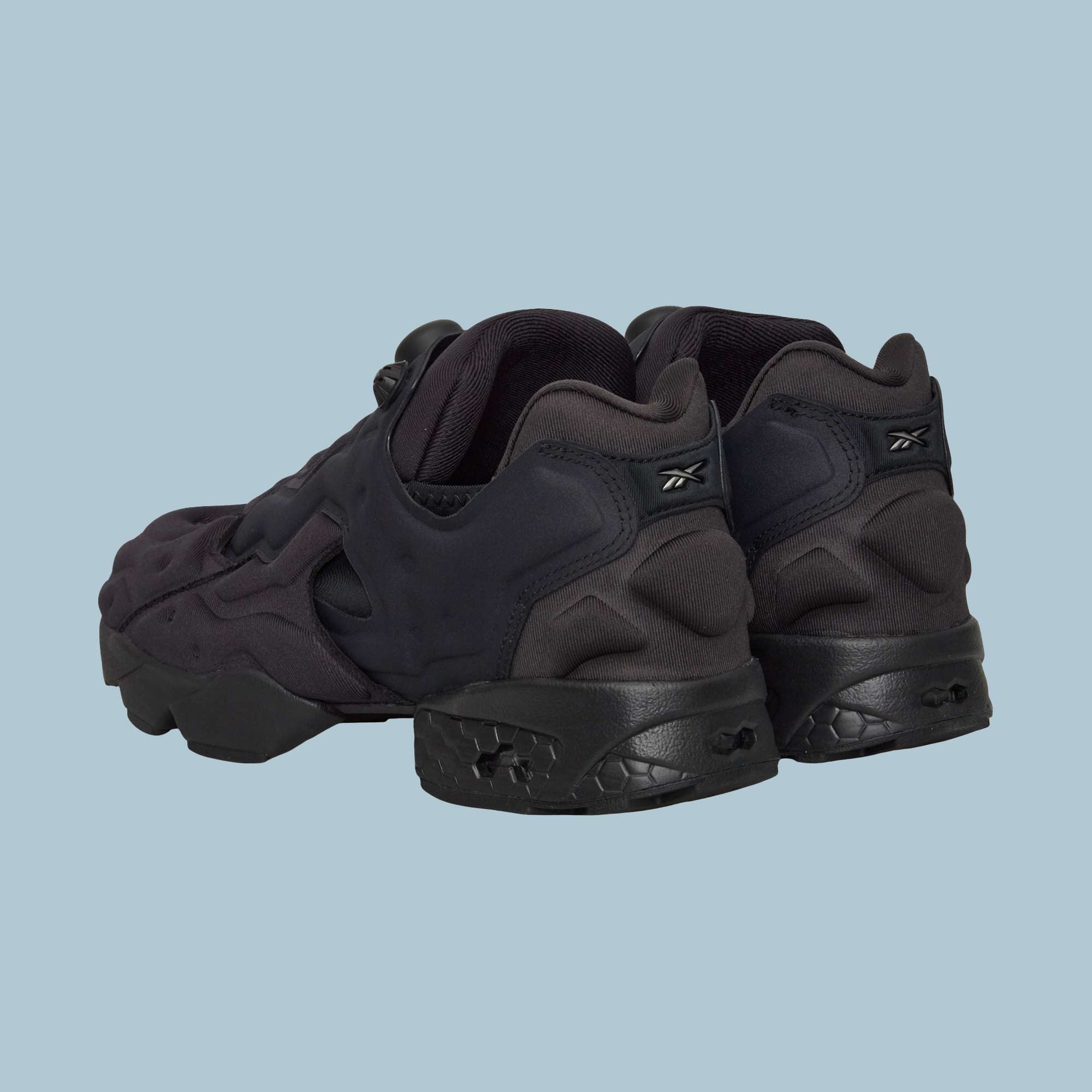 A pair of Reebok Instapump Sliver Shoes in black, featuring chunky design, textured soles, and Hexalite cushioning, displayed from the back and side on a plain light blue background.