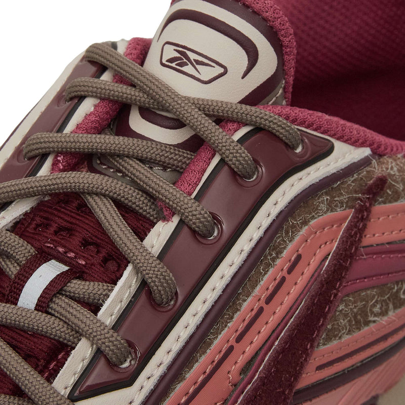 Close-up of the Reebok Premier Road Ultra Shoes featuring maroon, pink, and beige tones, logo on the tongue, gray laces, textured suede with glossy overlays, and a dual-density midsole for extra comfort.